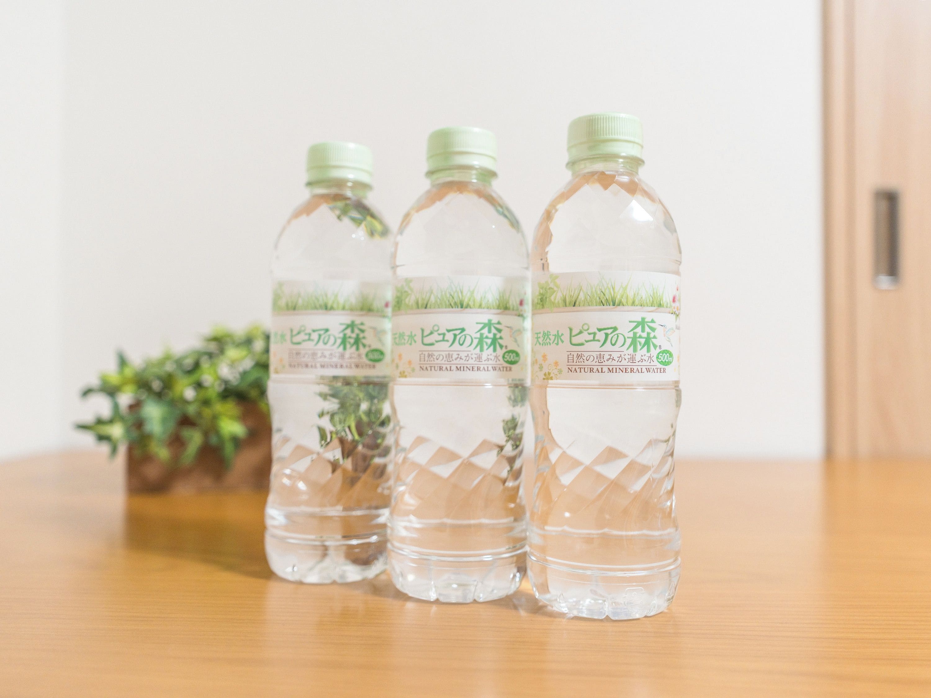 Tres botellas de agua con etiquetas sobre una mesa de madera, sobre un fondo liso.