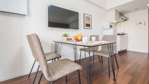 Un espace repas moderne avec une table ronde, quatre chaises rembourrées, un téléviseur à écran plat fixé au mur et une cuisine en arrière-plan.
