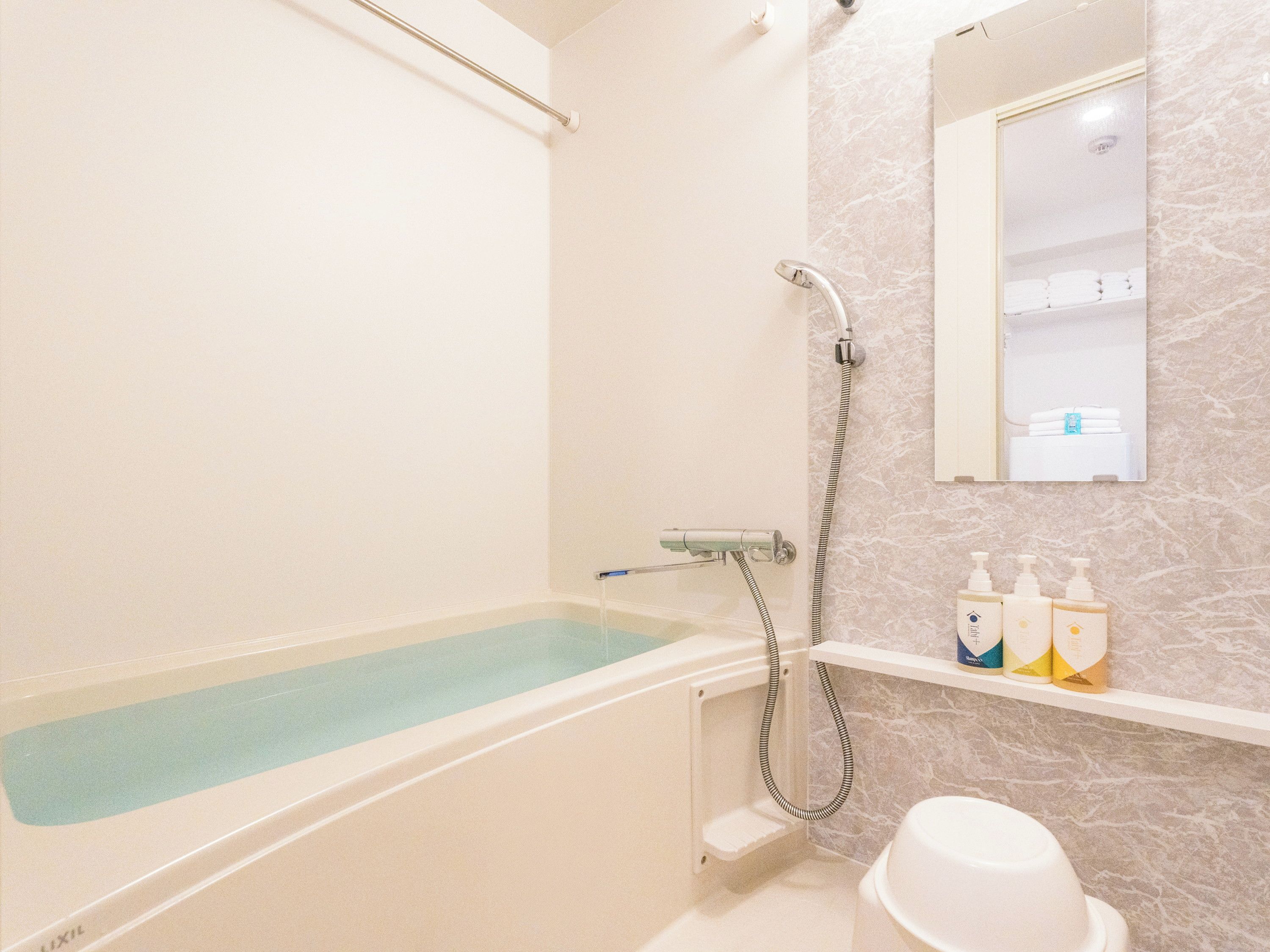 A bathroom with a bathtub, a shower, and a toilet. There are toiletries on a shelf.