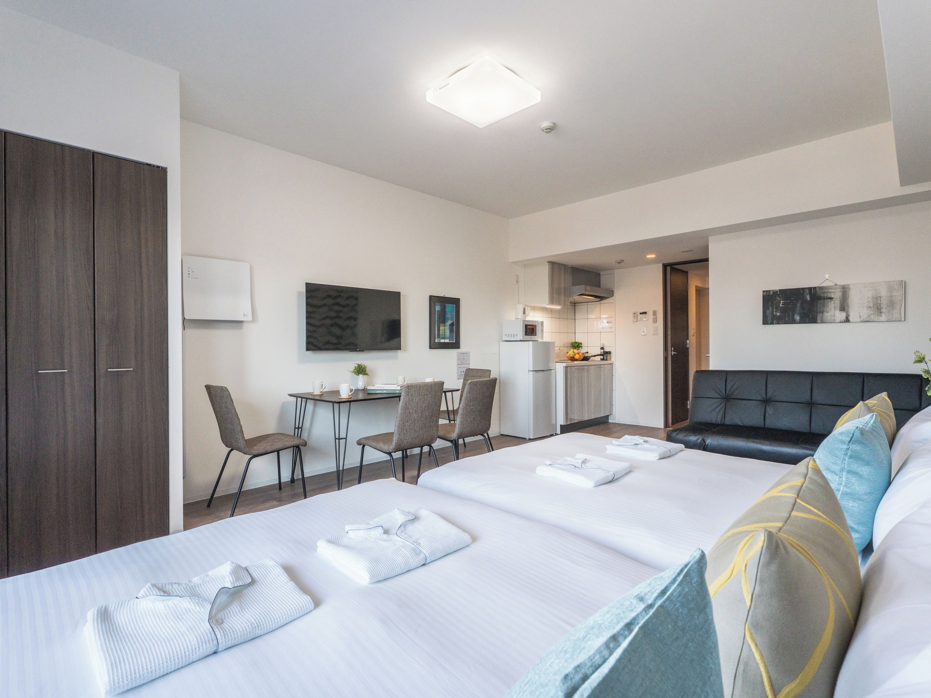 A hotel room with a bed, a desk, a kitchenette, and a TV.