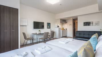 A hotel room with a bed, a desk, a kitchenette, and a TV.