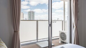 Une chambre d’hôtel avec une porte-fenêtre coulissante donnant sur un balcon, un lit et une fenêtre offrant une vue sur le paysage urbain.