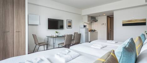 Habitación de hotel con dos camas, zona de comedor, cocina y televisor.