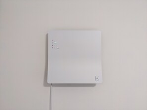 Dispositivo electrónico blanco con botón de encendido, sensor de calidad del aire y un logo en la esquina inferior derecha.