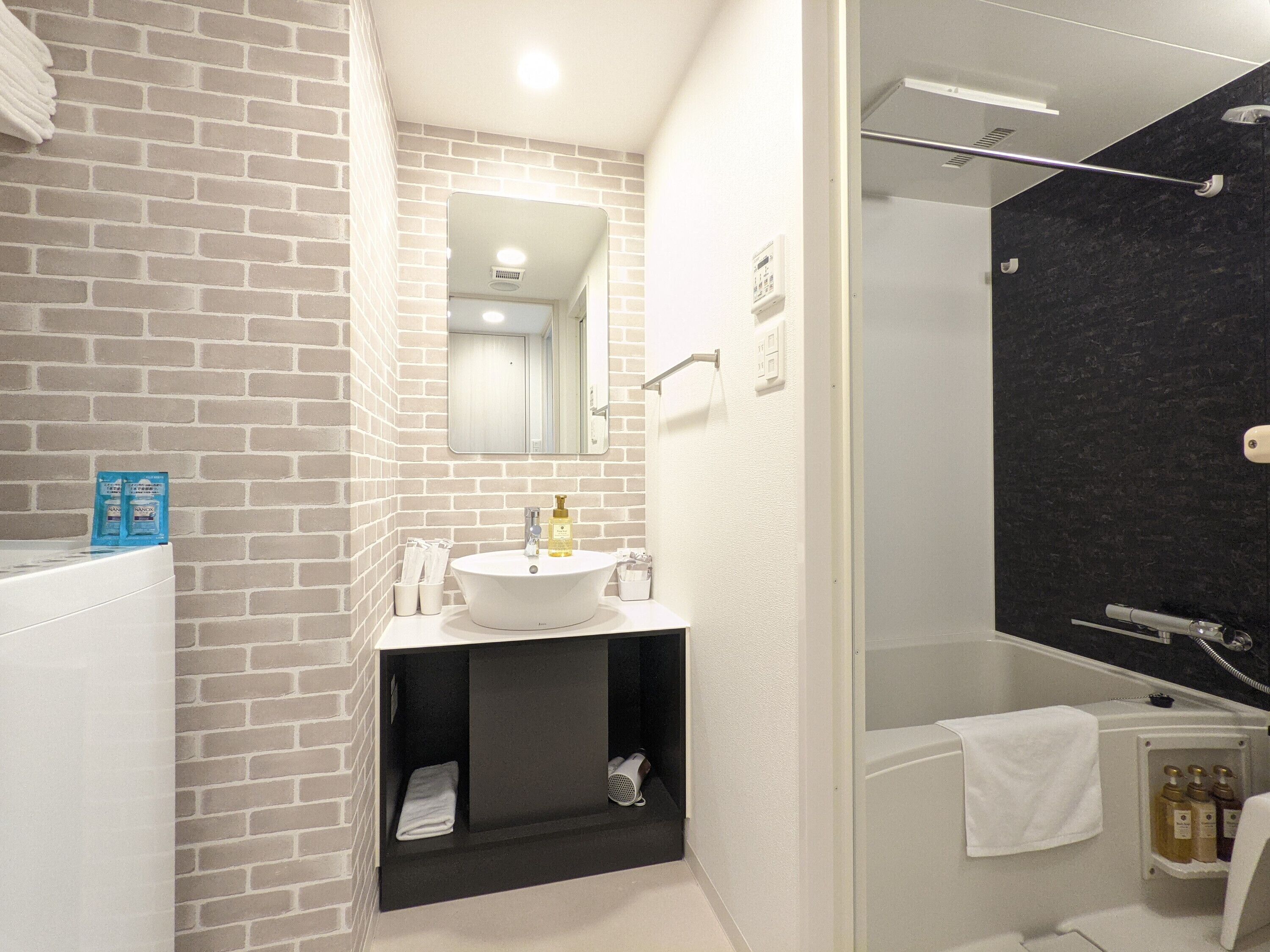 A modern bathroom with a brick wall, a white sink, a mirror, and a shower area.