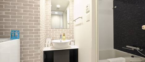 A modern bathroom with a brick wall, a white sink, a mirror, and a shower area.
