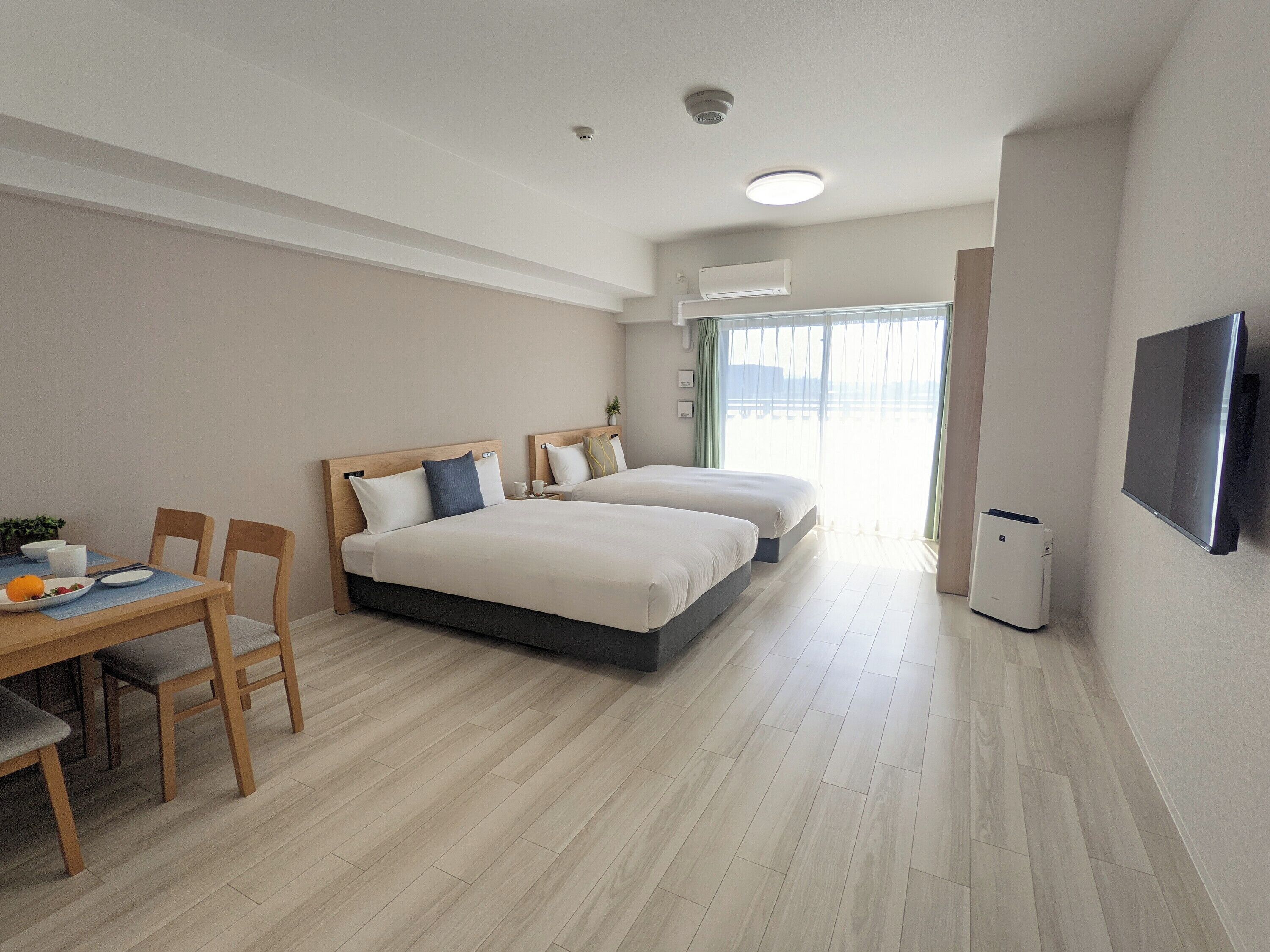 Een hotelkamer met twee bedden, een eettafel met stoelen, een televisie en een raam met gordijnen.