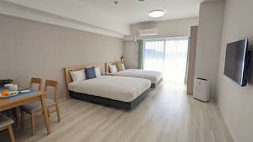 Een hotelkamer met twee bedden, een eettafel met stoelen, een televisie en een raam met gordijnen.