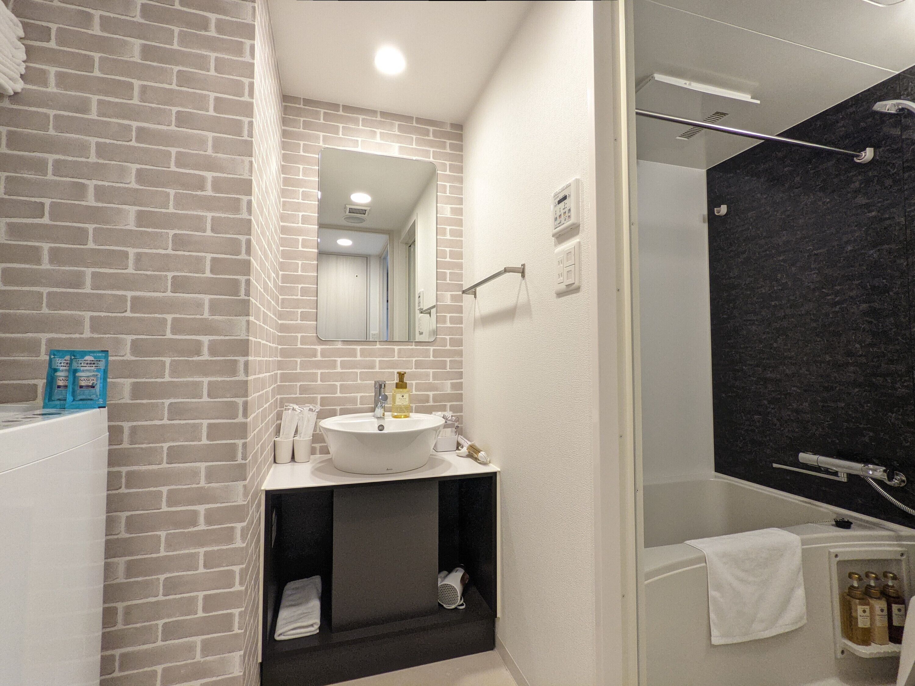A modern bathroom with a brick wall, a white sink, a mirror, a shower area, and a towel rack.