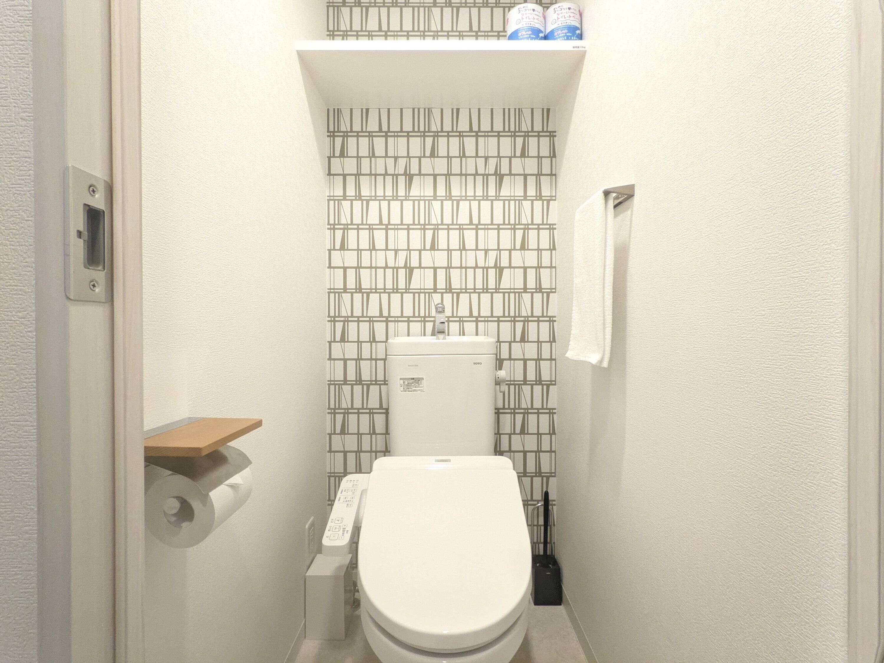 A compact bathroom with a toilet, a toilet paper holder, and a shelf with toiletry items.