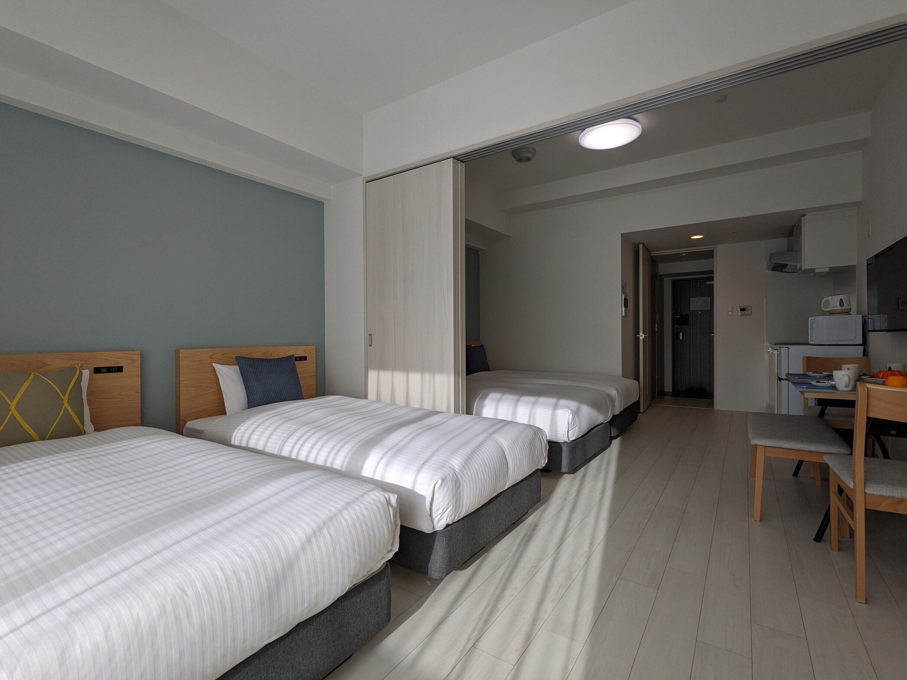 A hotel room with two beds, a desk, and a kitchenette.
