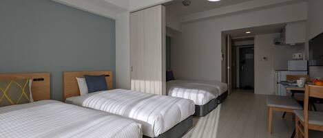 A hotel room with two beds, a desk, and a kitchenette.