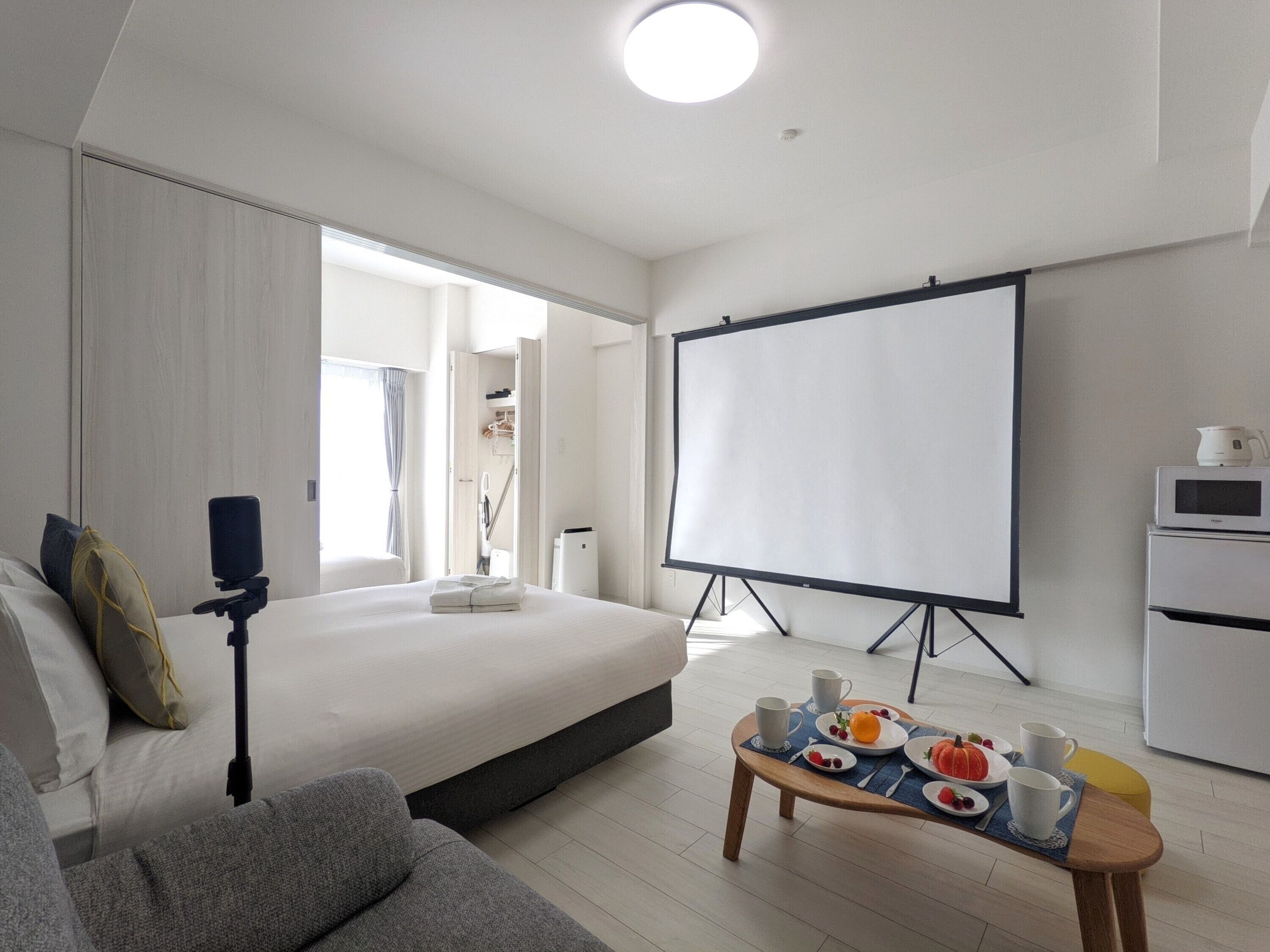 Una habitación de hotel moderna con una cama grande, una pantalla de proyector, una mesa de centro con alimentos para el desayuno y un sofá.