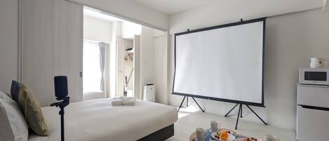 Una habitación de hotel moderna con una cama grande, una pantalla de proyector, una mesa de centro con alimentos para el desayuno y un sofá.