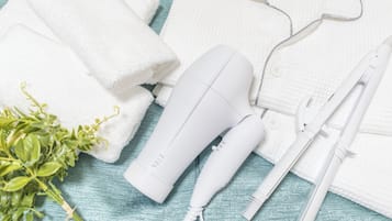 A white hair dryer, a white towel, a white shirt, and a pair of white scissors on a teal textured surface.