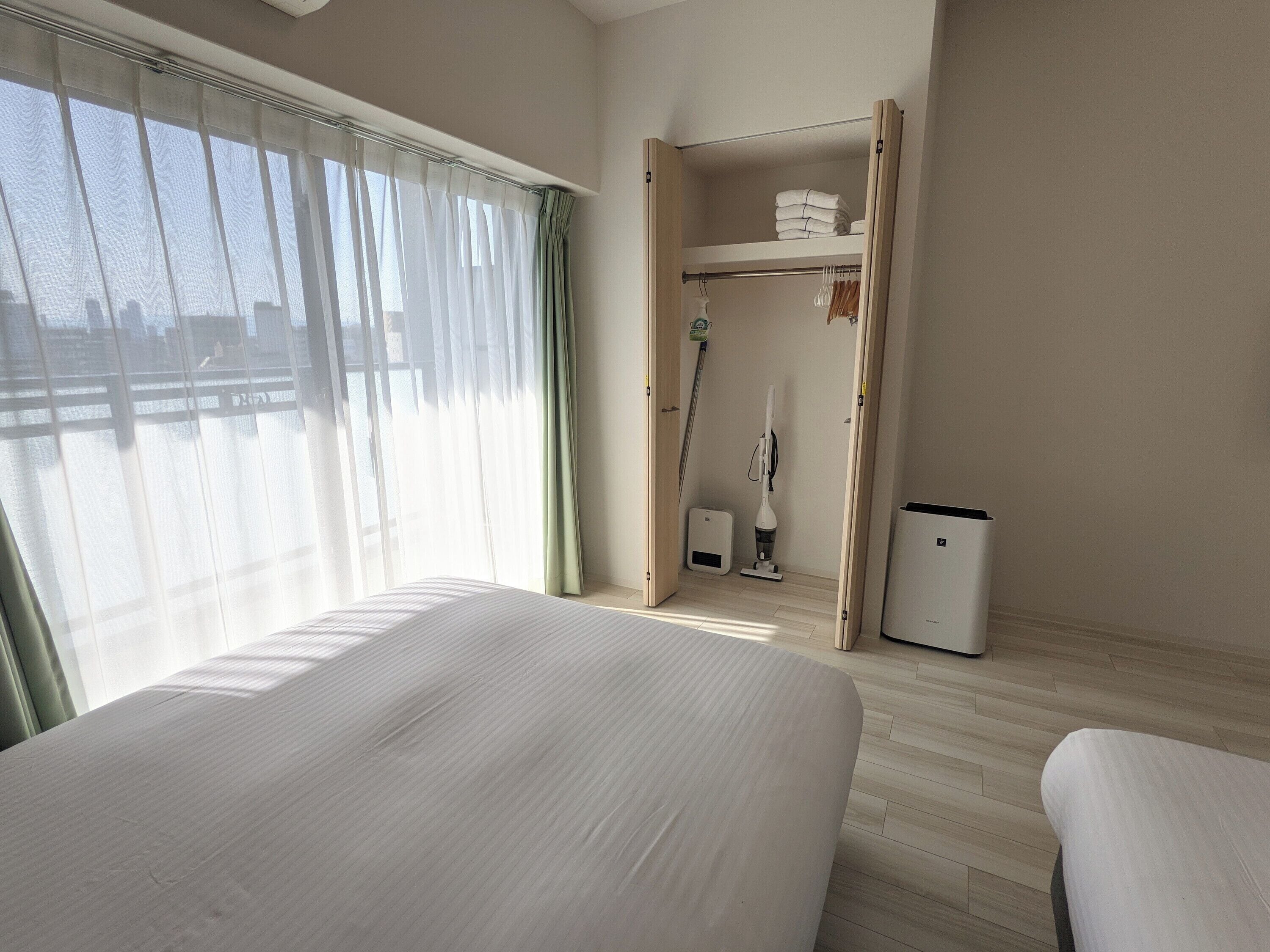 A hotel room with a bed, a wardrobe, a vacuum cleaner, and a heater.