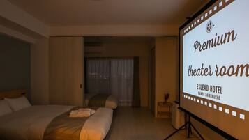 Habitación de hotel con una cama grande, una mesita pequeña y una pantalla proyectora mostrando el texto 'Premium theater room'.