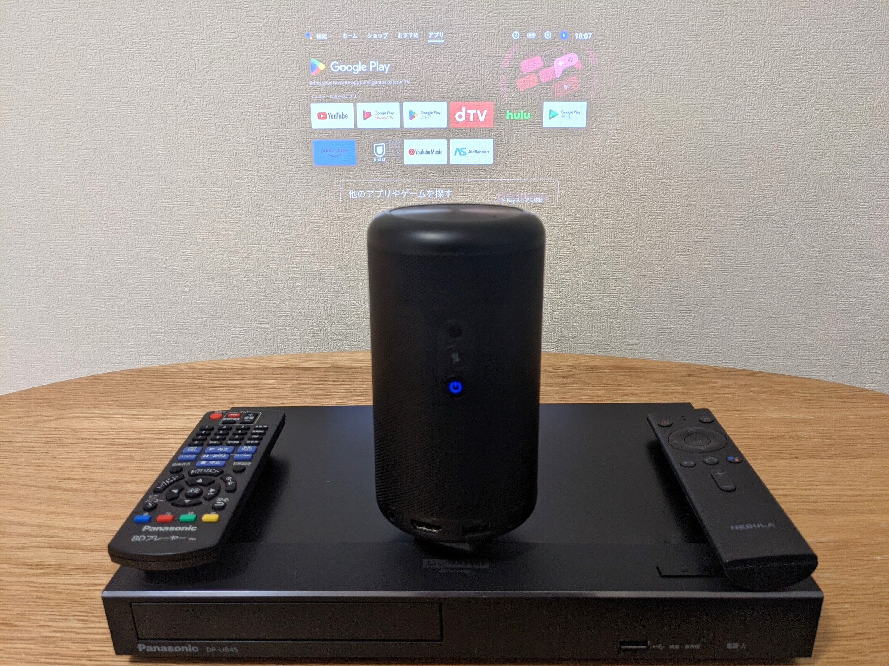 Un téléviseur Panasonic DP-UB45 posé sur une table en bois, avec une télécommande et un haut-parleur à proximité.