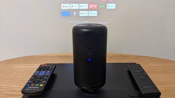 A Panasonic DP-UB45 TV on a wooden table with a remote control and a speaker.