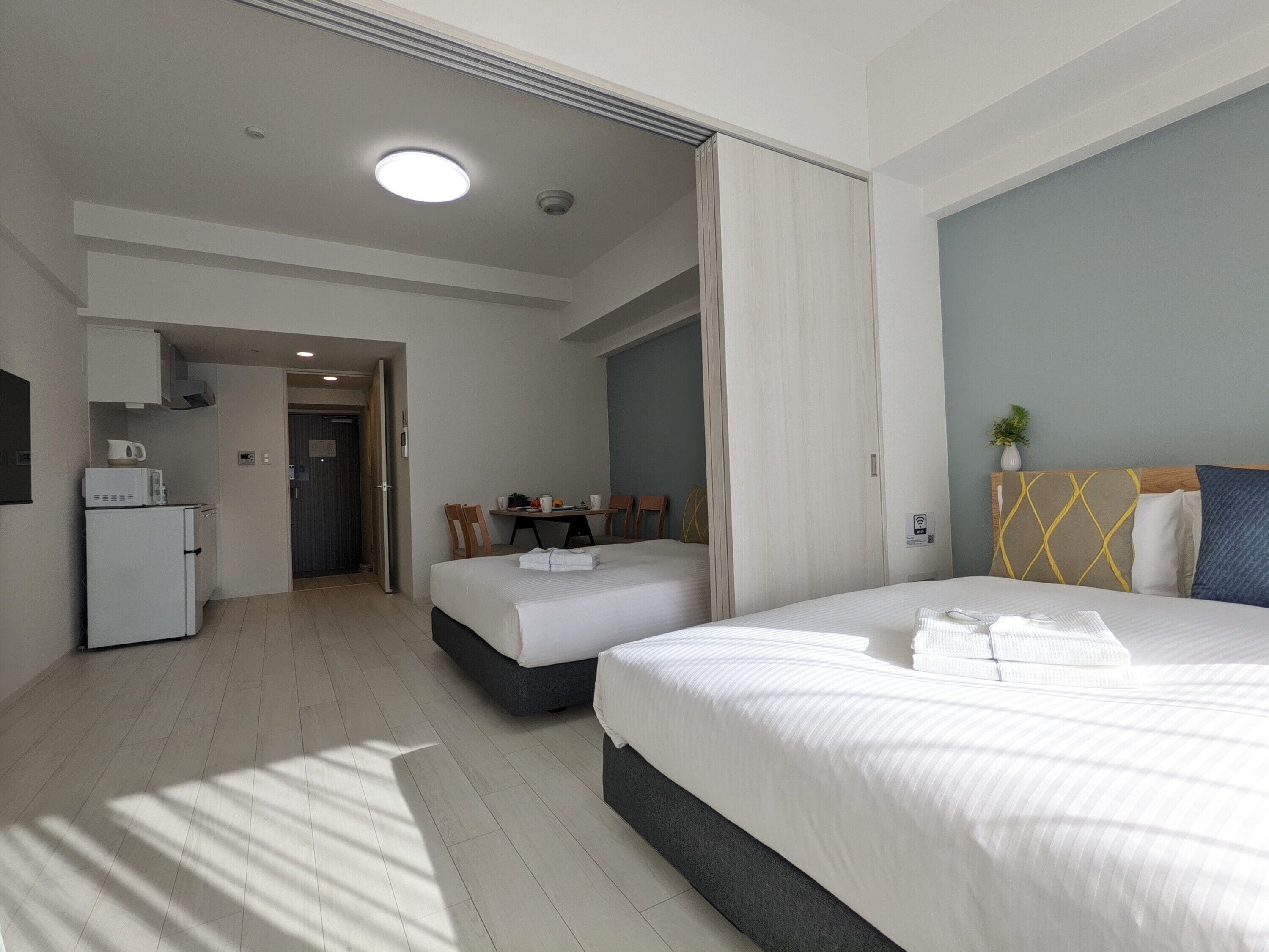 A hotel room with two beds, a kitchenette, and a dining area.