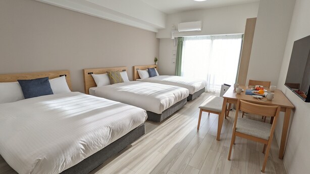 Quarto de hotel com duas camas, uma mesa de jantar e uma televisão.