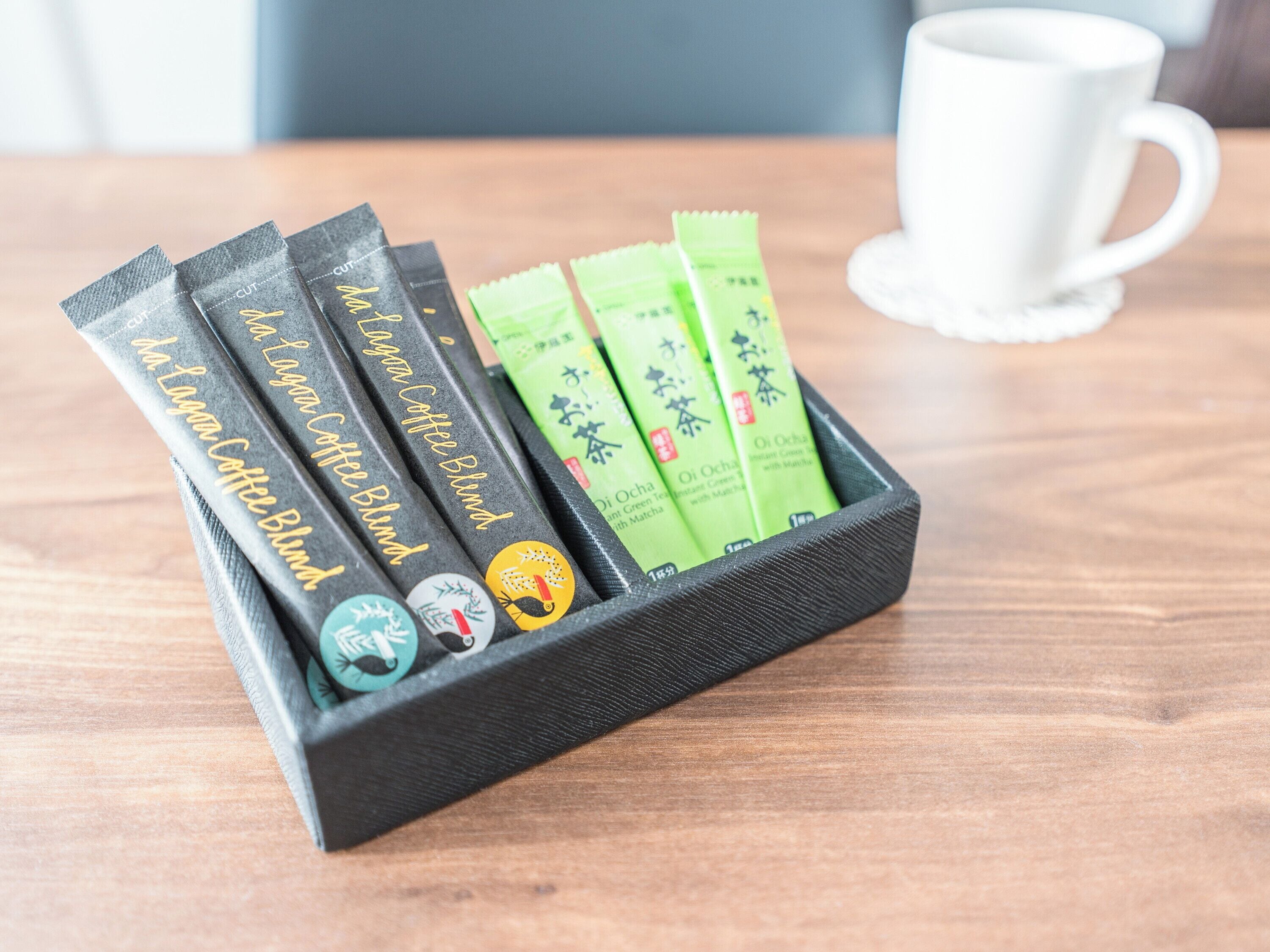 A black tray with tea packets and a white cup on a wooden table.