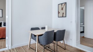Un coin repas minimaliste avec une table en bois et des chaises grises, un mur blanc et un tableau abstrait encadré.