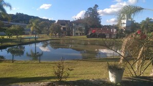 A serene outdoor setting with a pond, grassy areas, and buildings in the background. - Imperial Parque Hotel (Nova Petropolis)
