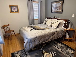 A bedroom with a bed, a chair, a bedside table, a lamp, and a window with curtains. - Checkout this place!! Cindy and Rick will make your stay memorable! (Alma)