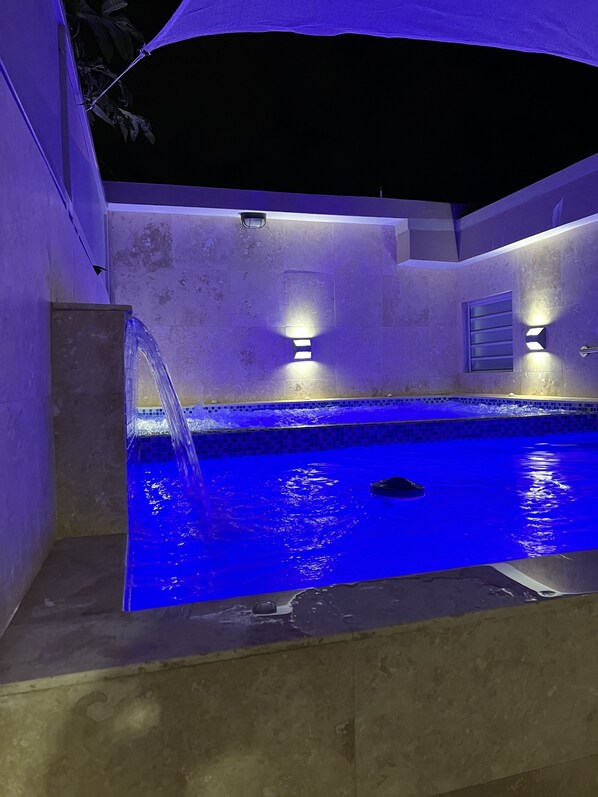 Una piscina amb una font, envoltada de murs amb superfícies rugoses i il·luminació integrada.