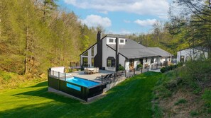 Una casa moderna de dos pisos con piscina, rodeada por un paisaje verde y exuberante.