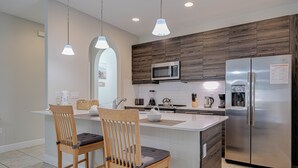Een moderne keuken met een centraal eiland, houten stoelen, een roestvrijstalen koelkast en een magnetron.
