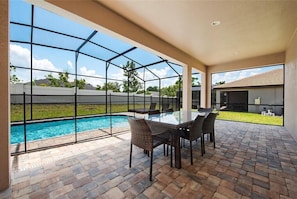 Une terrasse couverte avec une structure en verre, une piscine et un coin repas aménagé avec des meubles en osier.