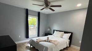 A bedroom with a bed, a ceiling fan, a window with curtains, and a door. - Azure Villa Sol (Lehigh Acres)
