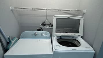 A compact laundry room with a front-loading washer and dryer, a metal drying rack, and a wall-mounted sign.