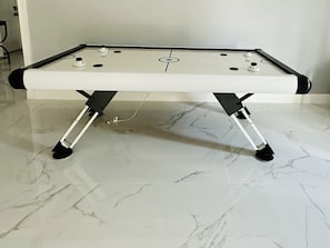 Una mesa de fútbol de mesa con superficie blanca y detalles negros, ubicada sobre un piso de mármol.
