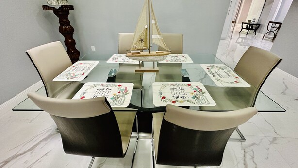 Una mesa de comedor con superficie de vidrio, rodeada por cuatro sillas y una decoración náutica de barco de vela.