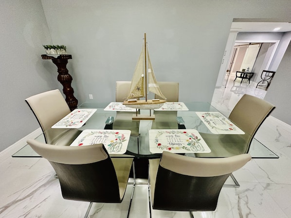 Una mesa de comedor con superficie de vidrio, rodeada por cuatro sillas y una decoración náutica de barco de vela.
