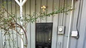 Uma trilha de pedra leva a uma porta preta, com um poste branco e uma pequena planta ao lado.
