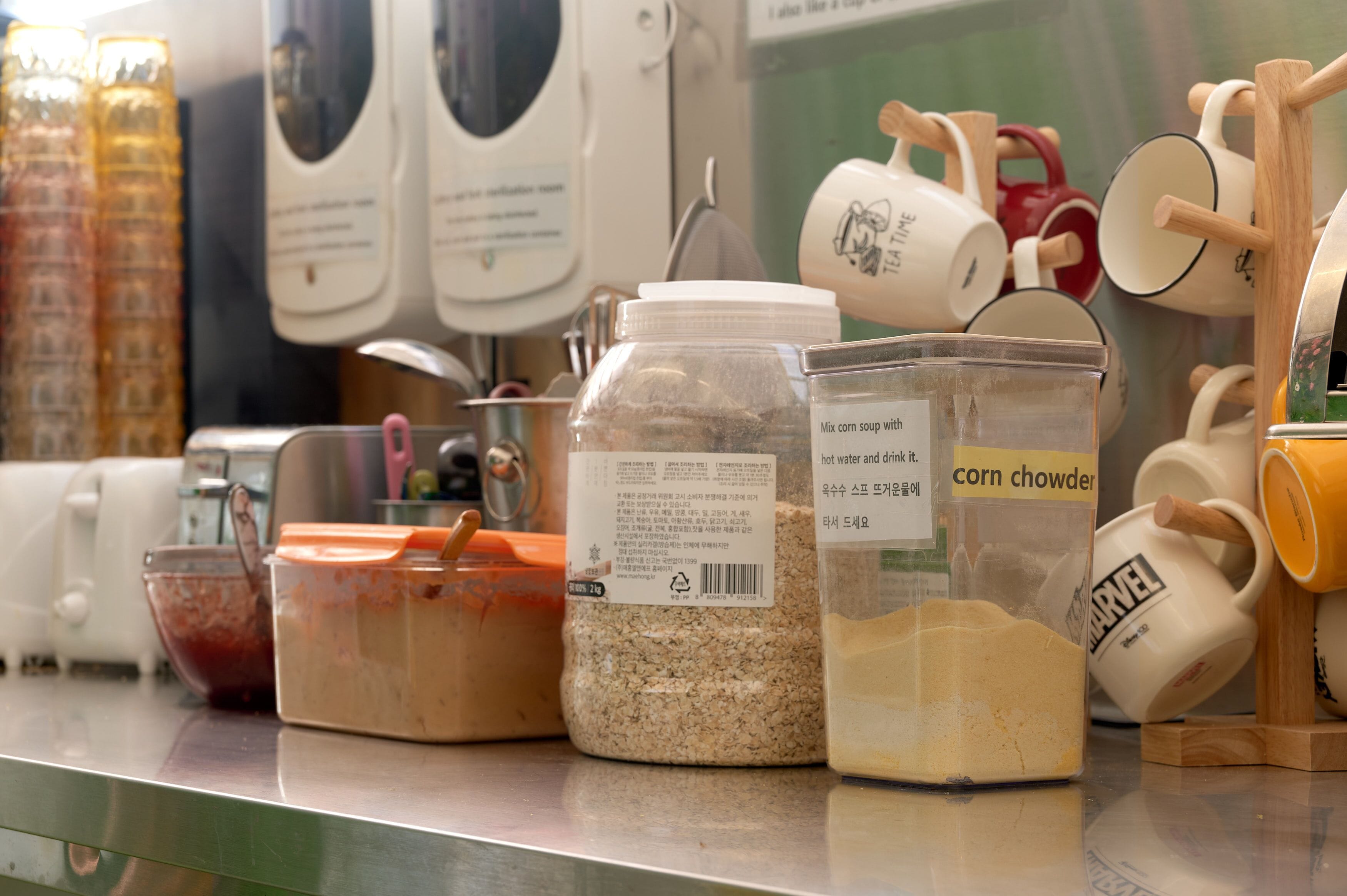 A kitchen counter with various food items and containers, including a jar labeled "corn chowder" and a container of oats.