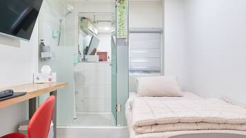 Quarto de hotel com cama, secretária e computador, uma cadeira, televisão e zona de duche.