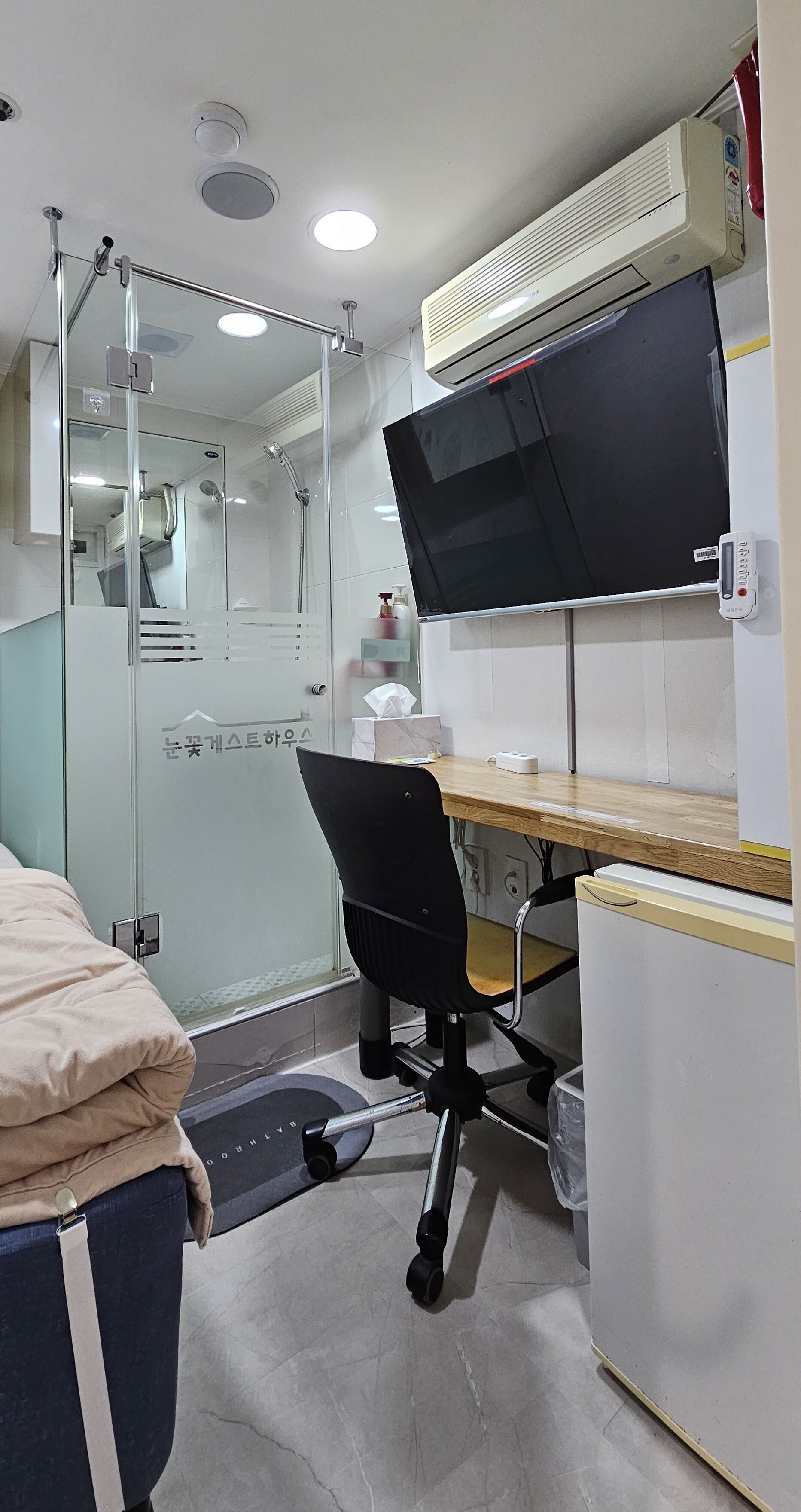 Un bagno compatto con doccia, water e lavabo. C'è una piccola scrivania con una sedia e una televisione montata sopra.