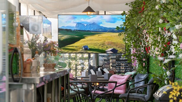 A cozy seating area with a table and chairs, a television displaying a scenic landscape, and a wall adorned with greenery and flowers. - Snowflower Guesthouse  (Seoul)