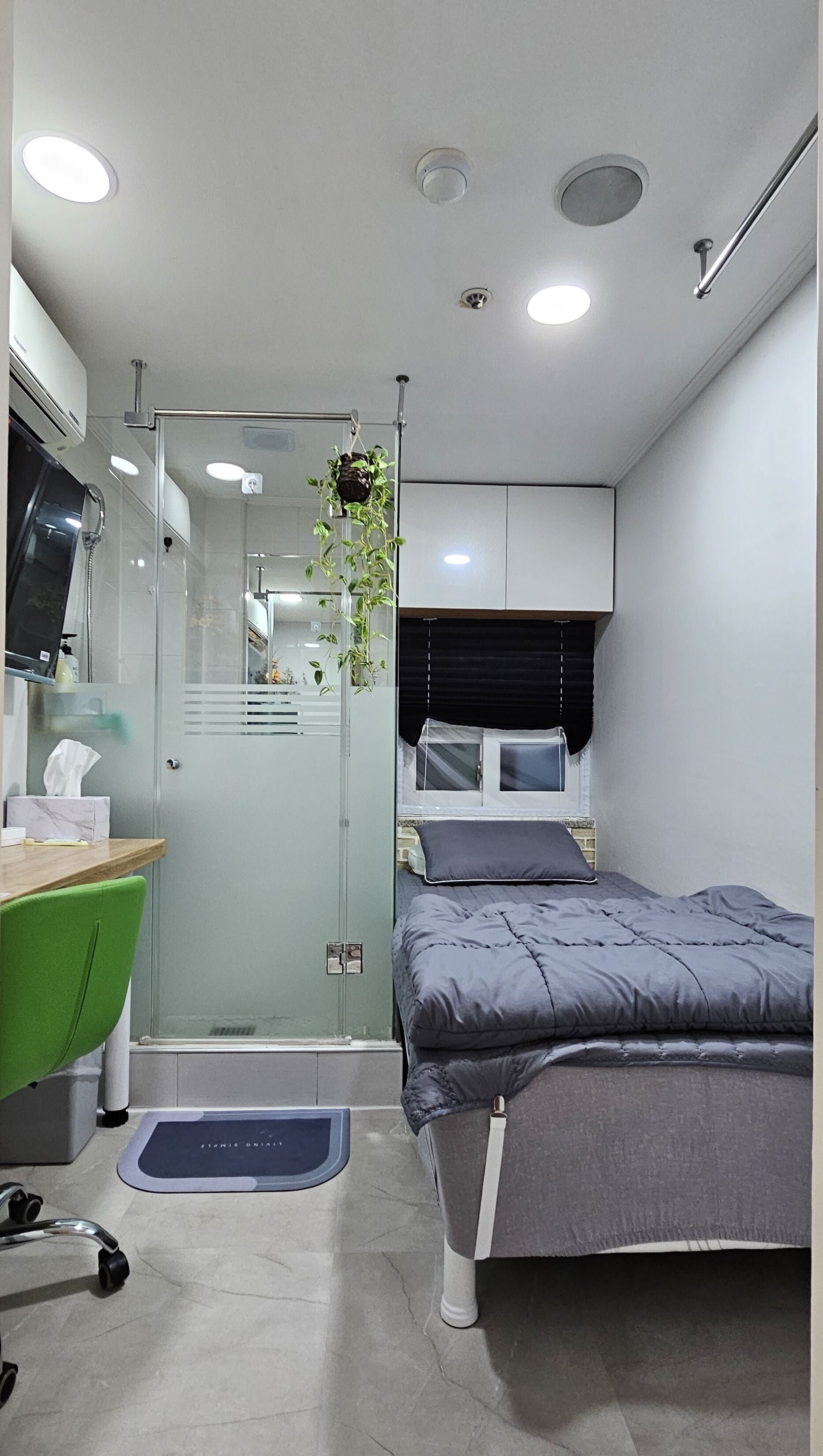 A modern bedroom with a bed, a desk, a chair, and a shower area.