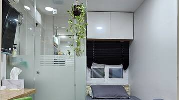 A modern bedroom with a bed, a desk, a chair, and a shower area.
