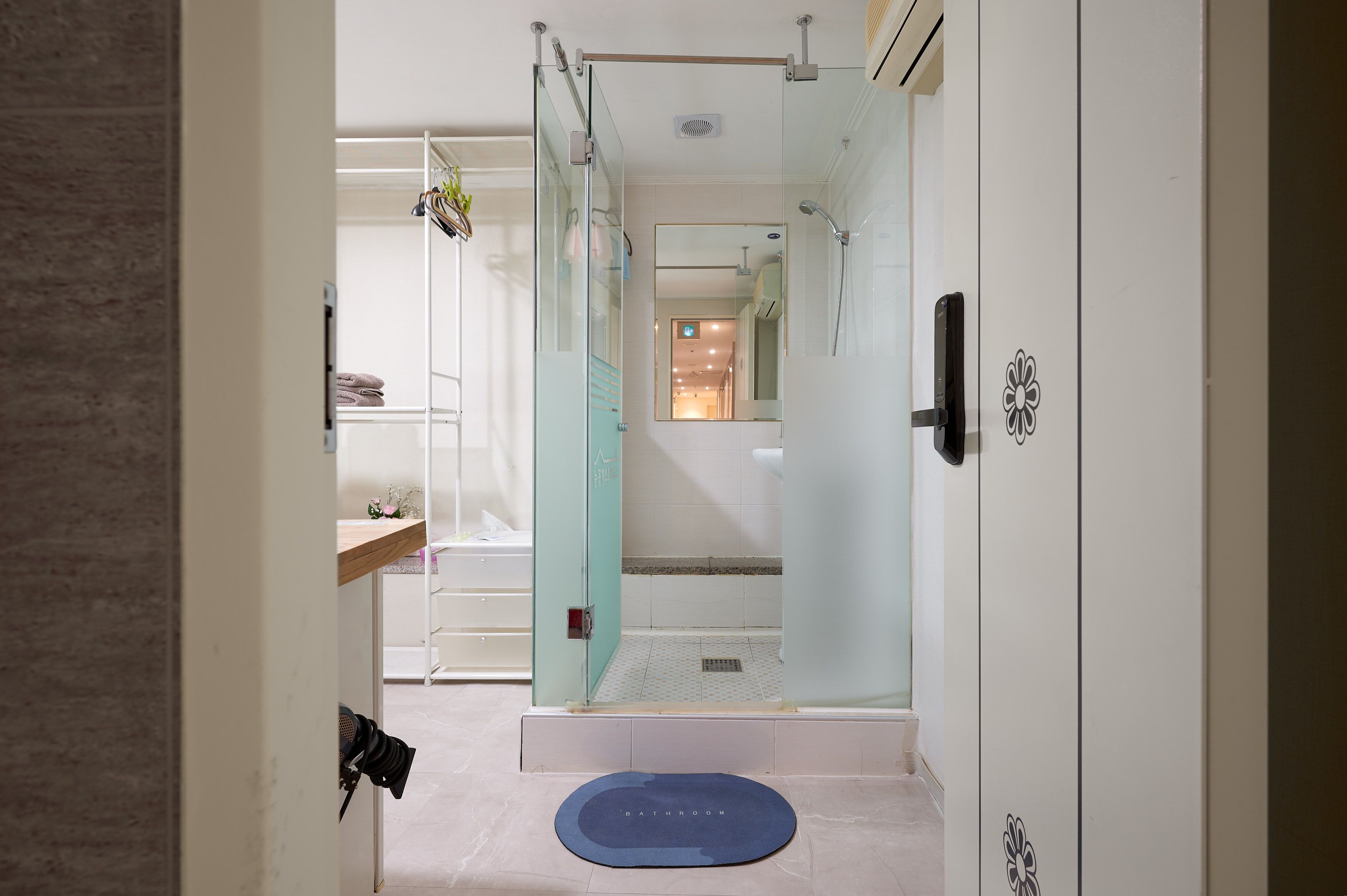 A modern bathroom with a glass shower enclosure, a visible toilet, and a blue mat labeled "BATHROOM" on the floor.