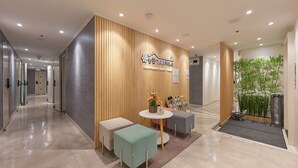 A modern reception area with a wooden panel wall, a reception desk, and two seating areas with a small table and flowers. - Snowflower Guesthouse  (Seoul)