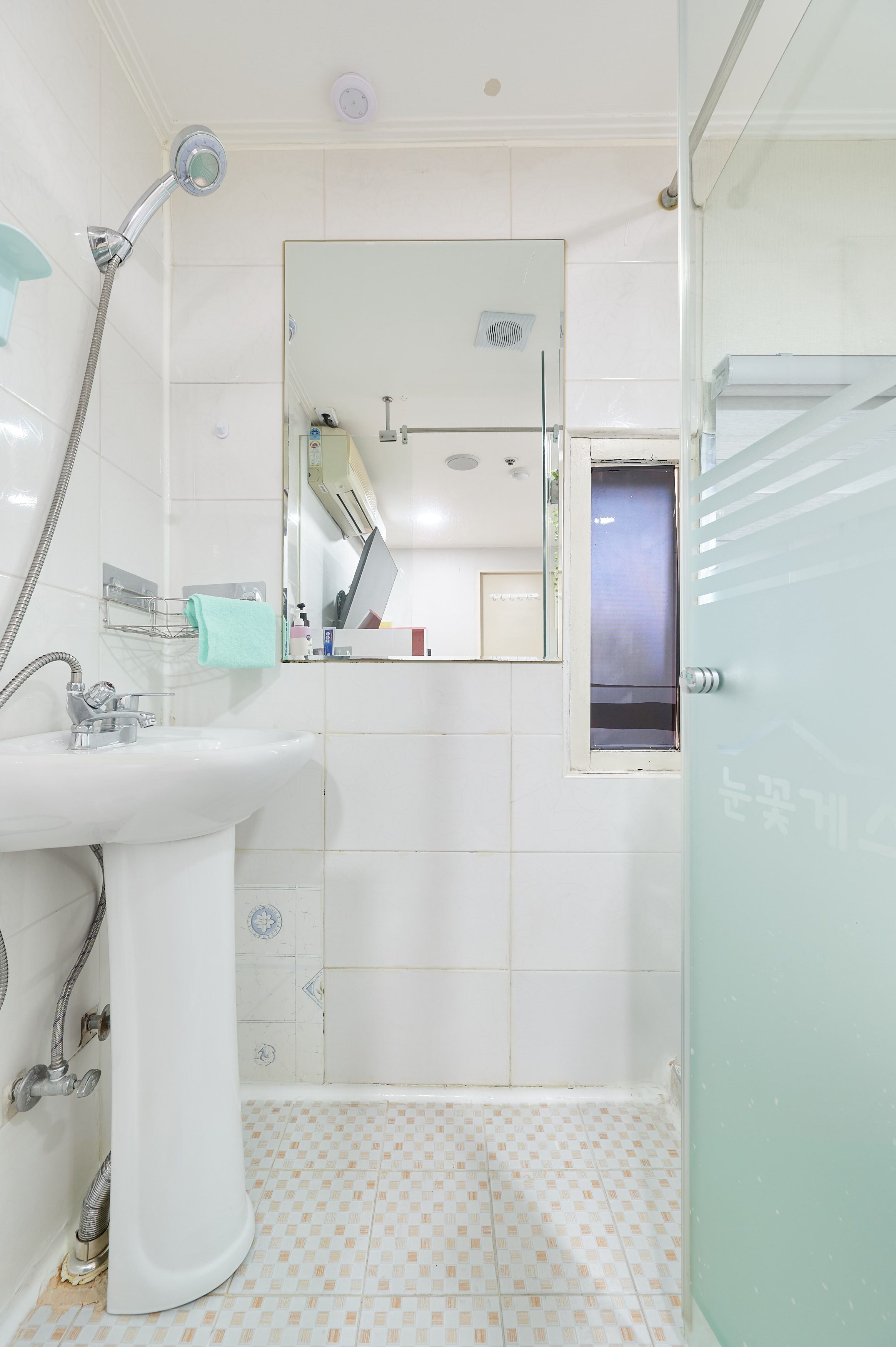 A bathroom with a sink, mirror, shower, and a door with a frosted glass panel.