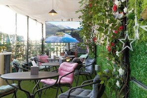 An outdoor seating area with tables and chairs, a large screen displaying a scenic view, and a wall decorated with greenery and flowers. - Snowflower Guesthouse  (Seoul)