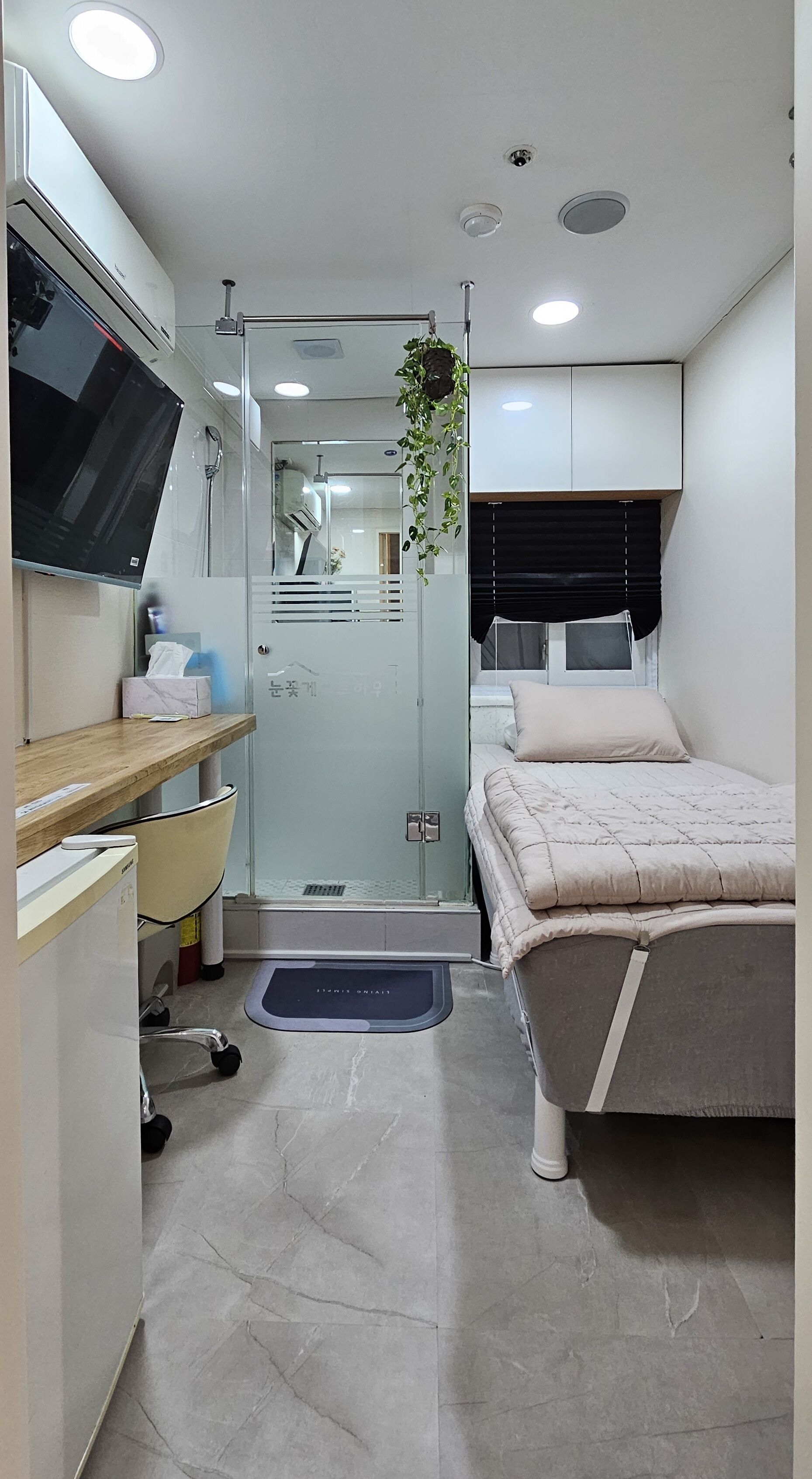 A compact bedroom with a bed, a desk, a chair, and a TV.